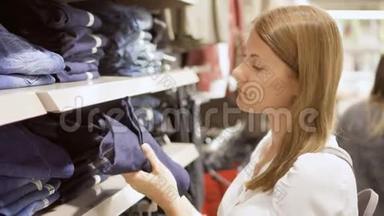 年轻女子在<strong>商场</strong>购物。 站在货架旁边，衣服拿起牛仔裤<strong>感</strong>觉材料