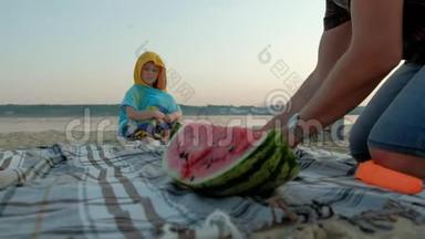 快乐的女孩在海滩上吃西瓜片。 父亲切西瓜夏天在户外野餐。