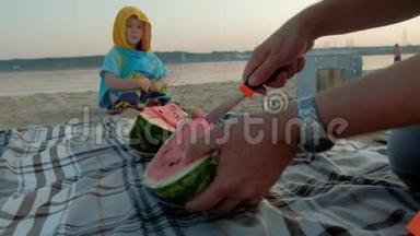 快乐的女孩在海滩上吃西瓜片。 父亲切西瓜夏天在户外野餐。