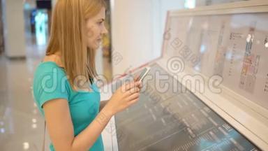 漂亮的年轻女人穿着绿松石的t恤，在商场里有智能手机。 制作商场布局照片