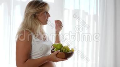 怀孕期间的饮食，大肚子的女孩拿着装有水果的木盘吃葡萄