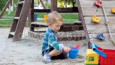 公园操场上可爱的幼儿男孩挖沙和倒塑料桶的慢动作视频