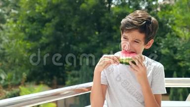 男孩少年在外面吃西瓜，背景是绿色和天空。 4k.慢动作。