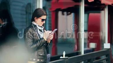 美丽的年轻黑发女子在城市街道背景下的智能手机上发信息