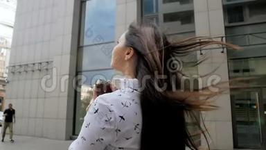 在刮风的日子里，一位留着长发的年轻美女在街头拍照片
