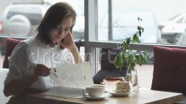 年轻的女商人在一家咖啡馆午休时休息，翻阅着`家时尚杂志