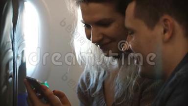 年轻漂亮的夫妇一起坐飞机旅行。 快乐的男人和女人使用智能手机，计划去看风景。