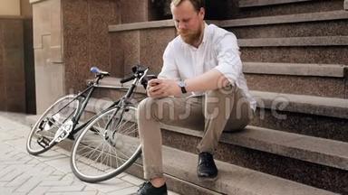 慢动作视频：一个满脸胡须的年轻人坐在街上的楼梯上，在智能<strong>手机</strong>上<strong>输入</strong>信息