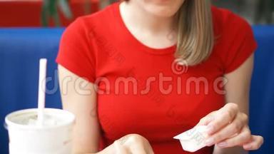 一位饥饿的年轻女士穿着红色T恤，坐在咖啡馆里吃着炸薯条，蘸着酱汁