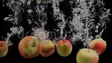 鲜红色和黄色的苹果落在溅出的水中，被隔离在黑色的背景上