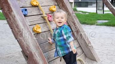 欢快的、微笑的幼儿男孩在操场上用木墙攀爬的慢动作视频