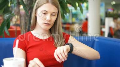 穿着红色T恤的女人用智能手表坐在咖啡馆里，和吃薯条的朋友聊天