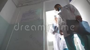 两位白种人的男医生从柜子里出来观看核磁共振成像，在x光上互相显示一些东西，然后移动
