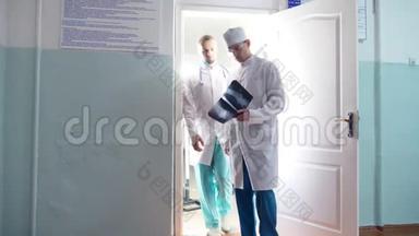 两位白种人的男医生从柜子里出来观看核磁共振成像，在x光上互相显示一些东西，然后移动