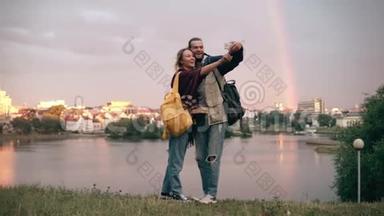 年轻的幸福<strong>夫妇</strong>拍摄的<strong>自拍照</strong>片与彩虹，近河的背景。 微笑的男人和女人使用智能手机