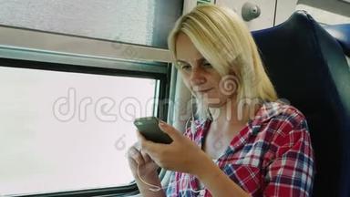 一个年轻的女人坐在火车的二楼，坐在窗边。 使用带耳机的智能手机