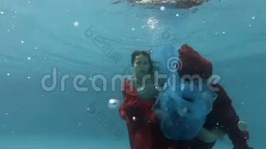 这个十几岁的女孩游泳，在池底用一块红色和蓝色的布水下玩耍。