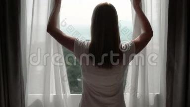 穿白色t恤的女人揭开窗帘，看着窗外。 在外面欣赏海景