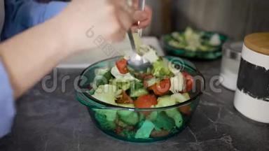 一个女人在厨房柜台上的<strong>玻璃碗</strong>里混合绿色新鲜<strong>蔬菜</strong>的特写镜头。