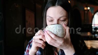 布鲁内特女士穿着格子衬衫，从一个大杯子里喝茶。 累的女人喝茶。