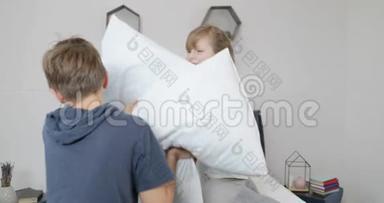 早上，幸福的一家人在卧室里，两个孩子在枕头上打架，幸福的微笑着的父母躺在床上
