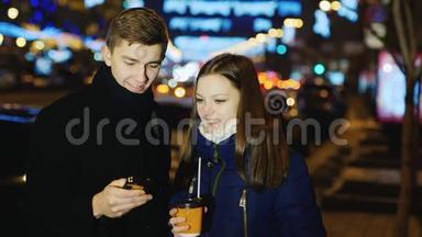 年轻人和女人在一条晚上的街道上说话，看手机`屏幕