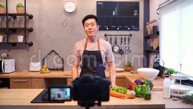 年轻的亚洲男人在厨房用<strong>相机录制</strong>视频。 微笑的亚洲男人在食品博客概念与水果和蔬菜