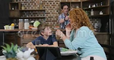母亲和儿子用平板电脑说话，父亲和女儿在厨房做饭，家庭幸福