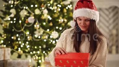 圣诞帽圣诞礼物盒和微笑的女人在圣诞树背景。 有着长长的黑发和圣诞老人的美丽的布鲁内特