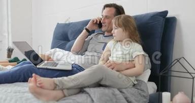父亲拥抱女儿谈电话，一<strong>起坐</strong>在床上，在卧室里用笔记本电脑