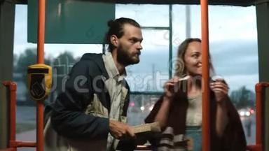 年轻的幸福夫妇站在公共交通工具里，坐电车。 女人带着票去运输，男人在等着。