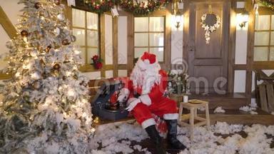 圣诞老人坐在房子附近的圣诞树之间，喝牛奶，吃饼干，听乙烯基的圣诞歌曲