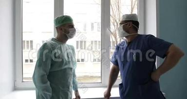 两名穿着制服和口罩的年轻医生正对着窗户在医院里交谈。