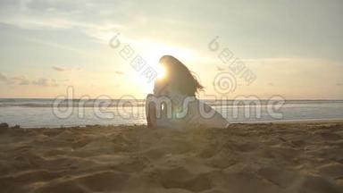 日落时分，美丽的年轻女孩坐在海边。 坐在海边金色沙滩上的女人