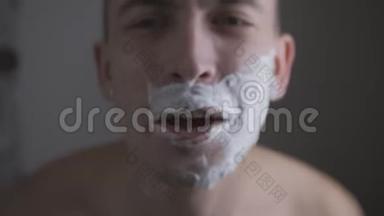 一个男人用剃刀在镜子前刮胡子，唱歌
