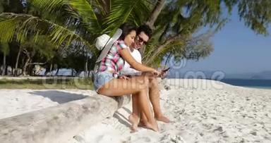 情侣用手机聊天<strong>坐在</strong>棕榈<strong>树下</strong>的沙滩上快乐的微笑男人和女人