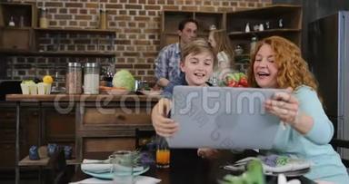 母亲<strong>和儿子</strong>一起举起手提电脑制作视频电话，让<strong>父亲和</strong>女儿<strong>在</strong>厨房做饭