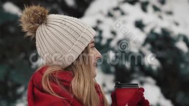 年轻漂亮的女孩穿着温暖的衣服站在圣诞树附近，在雪地里喝着报纸上的<strong>热饮料</strong>