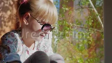 一个戴太阳镜的6岁女孩看着窗外。 窗外是春天，树皮的桦树枝，太阳是