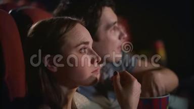 年轻夫妇在电影院欣赏电影。 两个人吃爆米花看电影