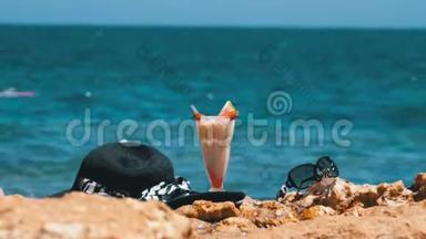 埃及海滩上的热带鲜榨果汁、帽子和眼镜架在红海边的岩石上