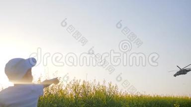 飞机在<strong>晴朗</strong>的天空中飞过田野的花朵，小男孩在草地上举手飞翔的直升机，小男孩坐着