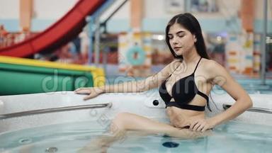 戴眼镜的年轻女人在按摩浴缸里放松，在相机前摆姿势。 漩涡浴池中女孩的肖像
