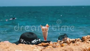 埃及海滩上的热带<strong>鲜榨果汁</strong>、帽子和眼镜架在海边的岩石上