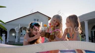 快乐的童年，被宠坏的孩子在充气床垫上带着彩色鸡尾酒，穿泳衣的小女孩在附近玩得很开心