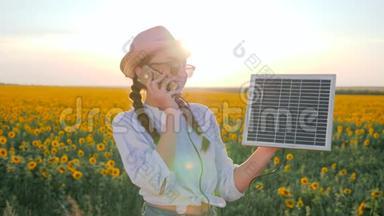 女孩用手机说话，拿着太阳能电池板在向日葵的背景地里，年轻女子拿着手机和太阳能