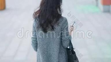 年轻漂亮的商务女孩，穿着严格的灰色夹克和黑色连衣裙，在城市忙碌中行走