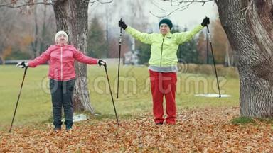 秋公园两位快乐的老年妇女在运动前做热身运动-北欧散步