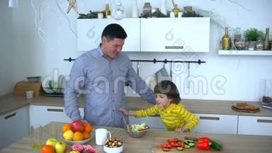 快乐的父亲和非常可爱的男孩在厨房准备蔬菜沙拉。 慢动作。 幸福家庭准备蔬菜
