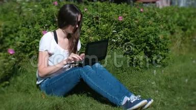 夏天，美丽的黑发女孩坐在公园里用笔记本<strong>电脑打字</strong>。
